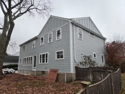 Front of the house mid-finish, boarded garage opening and siding debris in the drive